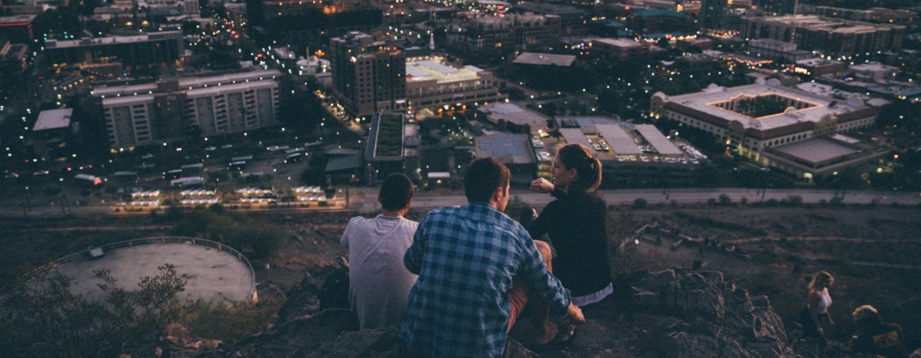 a group of people sitting on a hill overlooking a city